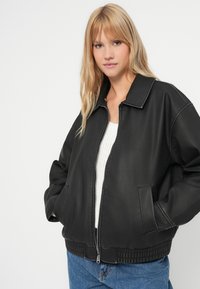 Μαύρο δερμάτινο τζάκετ bomber με φερμουάρ μπροστά, πλαϊνές τσέπες και ριμπ ελαστική μέση. Έχει γιακά και λεία υφή.