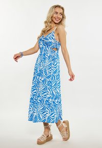 Rochie maxi cu un model floral albastru și alb, cu laterale tăiate, bretele ajustabile și o siluetă fluidă, asortată cu sandale cu talpă împletită.