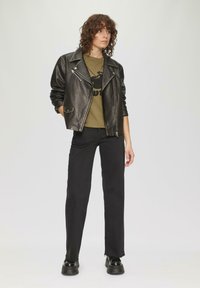 Zwarte leren motorjack met zilveren ritsen, olijfgroen graphic T-shirt, zwarte rechte broek en chunky zwarte schoenen.