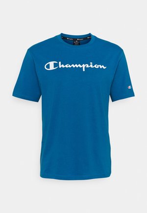 Niebieska koszulka z krótkim rękawem z białym logo "Champion" na piersi oraz małym logo Champion na lewym rękawie.