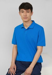 Blauwe polo met een knoopsluiting en korte mouwen, gemaakt van een katoenen mixstof, met een klein logo op de borst.