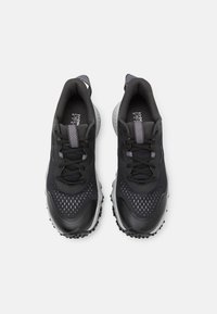 Chaussures de sport noires avec une tige en mesh, un capuchon de toe texturé et des semelles en caoutchouc. Présente des accents gris et des détails réfléchissants sur les lacets.