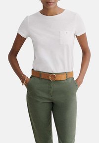 T-shirt blanc à manches courtes avec une poche avant, associé à un pantalon vert olive et une ceinture marron avec une boucle en métal.