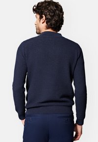 Granatowy sweter z teksturowanego dzianiny z okrągłym kołnierzem i ribbami na mankietach. Projekt charakteryzuje się subtelnym wzorem tkanym oraz dopasowanym krojem.