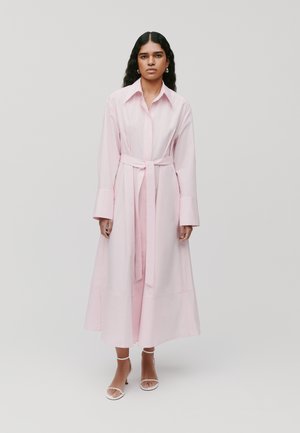 Lichtroze lange shirtjurk met een kraag, lange mouwen en een ceintuur om de taille. Beschikt over een vloeiende silhouet en een gladde stoftextuur.