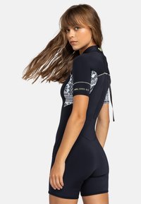 Combinaison de plongée à manches courtes en marine avec des panneaux à motifs. Comprend une fermeture éclair dans le dos et met en avant "Swell Series 2:2" sur le bras. Matière lisse et extensible.
