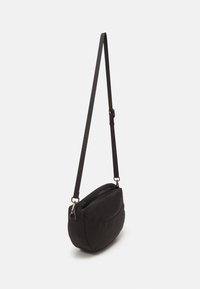 Sac bandoulière noir avec une forme arrondie et douce. Fabriqué en tissu au toucher lisse. Il possède une bandoulière réglable et une fermeture zippée.