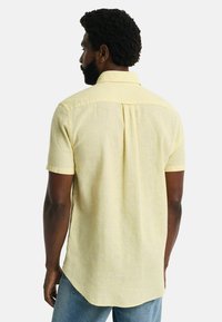 Kurzarmhemd aus leichtem gelben Leinen, mit einem Button-Down-Kragen, Rückenschlitz und abgerundetem Saum. Weiche Textur und lässige Passform.