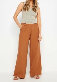 Jasnobrązowe spodnie z szerokimi nogawkami, wykonane z teksturowanej tkaniny, z elastycznym pasem i bocznymi kieszeniami, połączone z szarym topem bez rękawów.