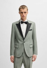 Completo verde chiaro con revers e tasca in raso nero, abbinato a una camicia bianca e a un papillon nero. Texture liscia e vestibilità su misura.