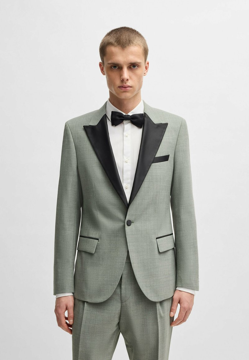 Completo verde chiaro con revers e tasca in raso nero, abbinato a una camicia bianca e a un papillon nero. Texture liscia e vestibilità su misura.