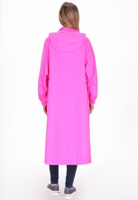 Hosszú rózsaszín esőkabát kapucnival, gumis mandzsettákkal és egyenes szabással. Kék farmerral és szürke, fémes részletekkel díszített cipővel viselve.