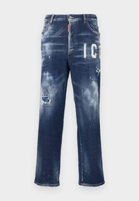 Vaqueros de mezclilla azul oscuro con parches desgastados, manchas de pintura claras y letras blancas en negrita. Diseño de pierna recta con un ajuste clásico.