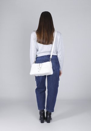 White faux fur handbag with a silver hardware accent, worn crossbody, paired with a gray long-sleeve top and blue denim cargo pants.
