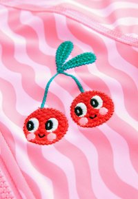 Różowa tkanina do kąpieli o falistym wzorze z czerwonymi haftowanymi wiśniami z uśmiechami, zielonymi liśćmi i kontrastującymi czarnymi oczami.