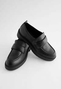 Black loafers made of smooth leather, featuring a wide strap across the front, thick rubber sole, and rounded toe design.