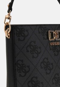 Czarna syntetyczna torebka z wzorem diamentowym, złotym wykończeniem i wyeksponowanym logo "GUESS" z ozdobnym łańcuszkiem na pasku.