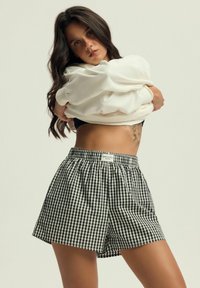 Czarno-białe szorty w kratkę o elastycznej talii z metką "Stay Cool". Połączone z białym, oversize'owym swetrem. Gładka tekstura materiału.