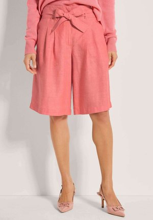 Rosa Leinen-Culotte-Shorts mit gebundener Taille, versehen mit vorne liegenden Falten und weiter Passform. Kombiniert mit hellrosa Schuhen mit Absatz.