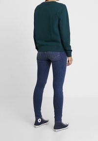 Sudadera verde con puños acanalados, combinada con jeans skinny azul oscuro y zapatillas altas marinas con un logo de estrella blanca.