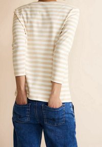 Randig topp med trekvartslånga ärmar i crème och ljusbeige, kombinerad med blå denimjeans med fickdetaljer.