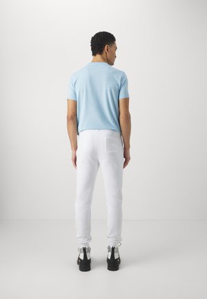 Light blue short-sleeve shirt paired with white sweatpants. The model wears black shoes with accents. Texture appears smooth and casual.