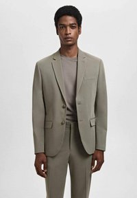 Light green suit jacket with two buttons, notched lapels, and a chest pocket, paired with a grey t-shirt. Plain, tailored fit.