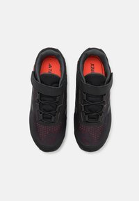Baskets de sport noires et rouges avec une tige en maille, texture tissée et une sangle à crochets et boucles. Comprend un embout renforcé et une semelle intérieure rembourrée.