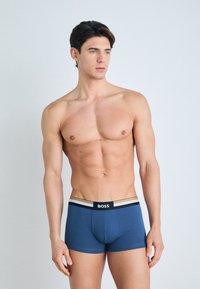 Navy blue boxer briefs made of elastic material with a black and beige striped waistband featuring the brand name "BOSS" in white.