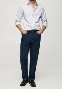 Camisa de manga larga con cuello, a rayas azul claro y blanca, combinada con jeans de mezclilla azul oscuro y zapatos de cuero negros.