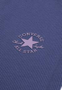 Μωβ υφασμα με ραβδώσεις που φέρει στρογγυλό, ροζ κεντητό λογότυπο με πεντάκτινο αστέρι, το κείμενο αναγράφει "CONVERSE Chuck Taylor ALL STAR."