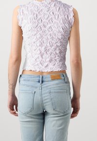Světle růžový cropped top s texturovaným křížovým vzorem, vlnkovým lemem a mírně vystouplými rukávy, spárovaný se světle modrými džíny.