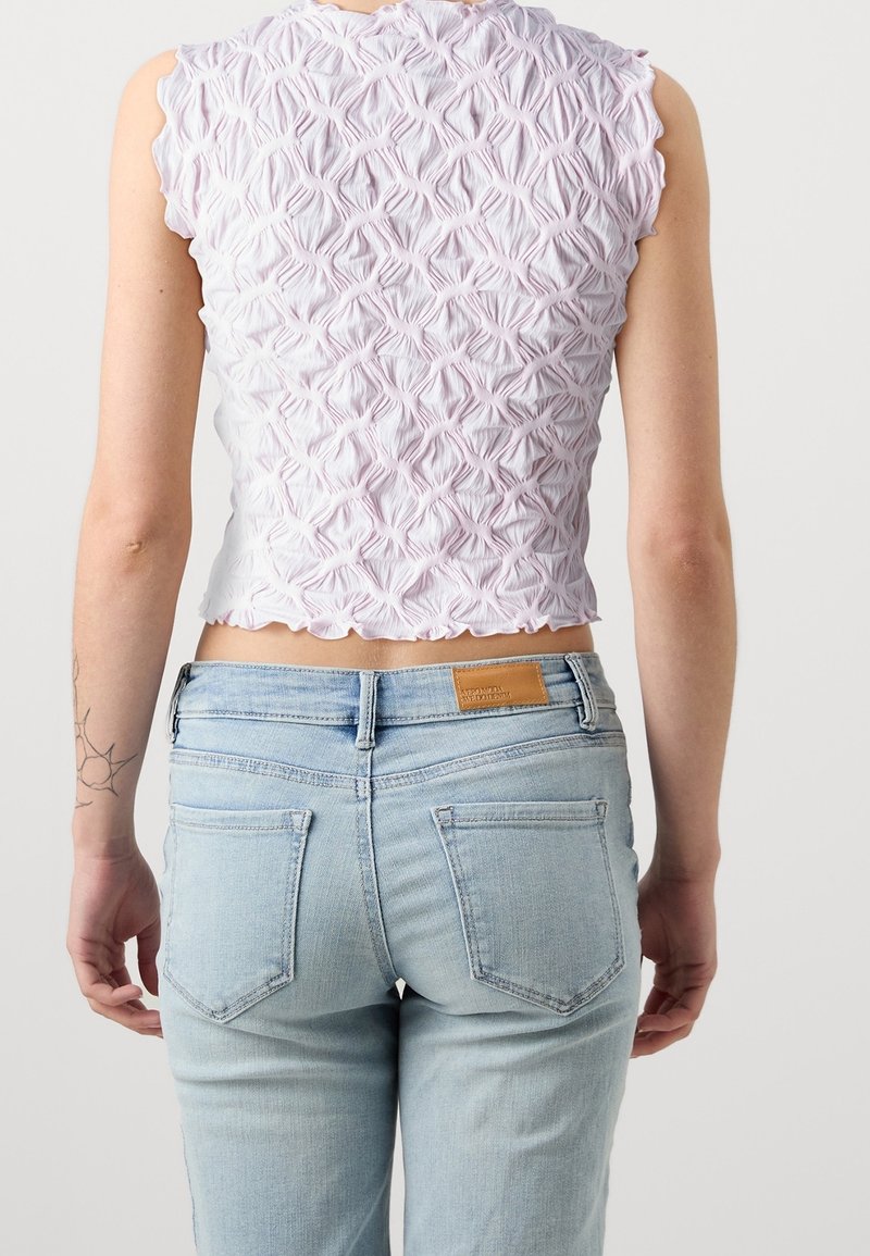 Světle růžový cropped top s texturovaným křížovým vzorem, vlnkovým lemem a mírně vystouplými rukávy, spárovaný se světle modrými džíny.