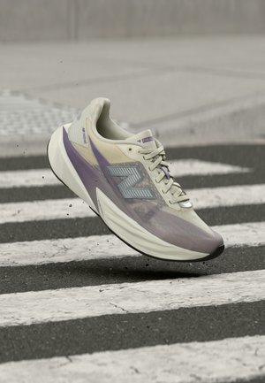 Lys lilla og beige løbesko med "N"-logo, der svæver over et sort-hvidt fodgængerfelt på asfalt.