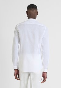 Camicia bianca a maniche lunghe in lino con colletto alla coreana, caratterizzata da un orlo dritto e polsini con bottoni. Tessuto leggero e traspirante con una texture morbida.