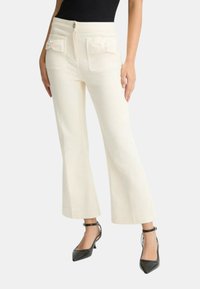 Pantaloni bianchi a vita corta con gamba larga, dotati di due tasche posteriori con dettagli a fiocco e chiusura frontale con bottone. Indossati con scarpe nere con tacco alto.