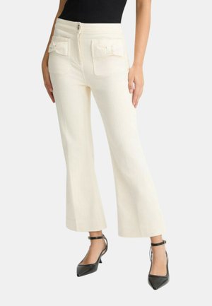 Pantaloni bianchi a vita corta con gamba larga, dotati di due tasche posteriori con dettagli a fiocco e chiusura frontale con bottone. Indossati con scarpe nere con tacco alto.
