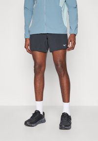 Schwarze Sportshorts mit einem seitlichen Logo, kombiniert mit einer hellblauen Jacke, weißen Socken und schwarzen Sneakers mit einer strukturierten Sohle.