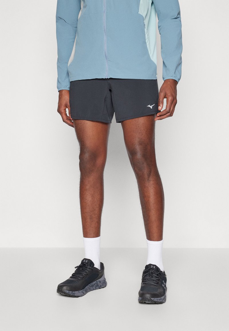 Schwarze Sportshorts mit einem seitlichen Logo, kombiniert mit einer hellblauen Jacke, weißen Socken und schwarzen Sneakers mit einer strukturierten Sohle.