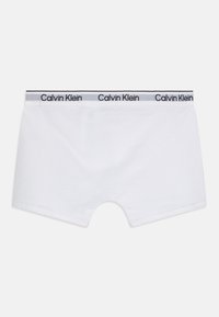 Hvite bomullsbokser med en grå linning som har gjentatt "Calvin Klein" tekst. Glatt tekstur og klassisk rektangulær form.