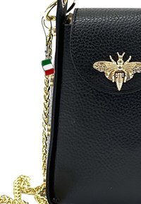 Zwarte leren tas met textuur en een gouden bij-embleem op de klep, evenals een kleine Italiaanse vlagcharme die is bevestigd aan een gouden schouderband.