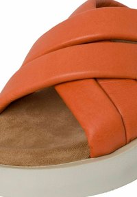 Sandale en cuir orange avec des sangles entrecroisées, intérieur en daim et semelle en caoutchouc beige épaisse. Texture douce et forme arrondie.