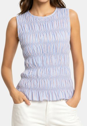 Top senza maniche azzurro con righe verticali rosa e tessuto arricciato, indossato con pantaloni bianchi, mani nelle tasche.