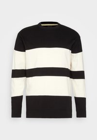 Jersey de rayas blancas y negras con cuello redondo; mangas largas; presenta audaces rayas horizontales de diferentes anchos. Textura de punto suave.