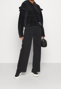 Svart velourkortad hoodie med volangärmar och framtida ficka, ihop med högmidjade svarta vida jeans och svarta sneakers.