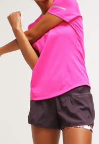 Klart rosa kortärmad träningströja i strukturerad tyg som matchas med mörkgrå shorts med Adidas-logotyp och färgglad insida.