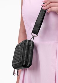 Schwarze gesteppte Handtasche mit silberner Hardware, doppelten Reißverschlüssen und einem abnehmbaren Tragegurt. Verfügt über eine glatte Textur und markante Akzentdetails.