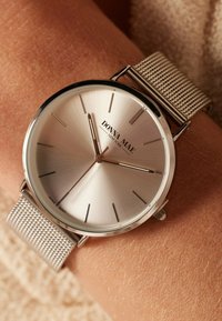 Silberfarbene Uhr mit einem Armband aus Edelstahl-Mesh. Das minimalistische Design verfügt über ein gebürstetes Zifferblatt und einfache Stundenmarkierungen, ohne Ziffern.