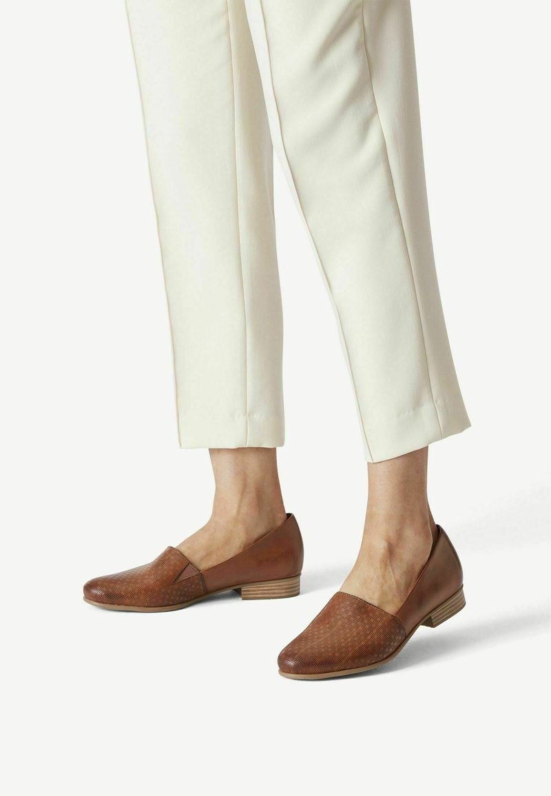 Mocassins en cuir marron à finition texturée, dotés d'un petit talon empilé et d'un design minimaliste. Portés avec un pantalon crème.