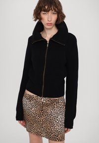 Svart ribbad stickad zip-up jacka med stor krage, kombinerad med en leopardtryckt minikjol med asymmetrisk fåll.